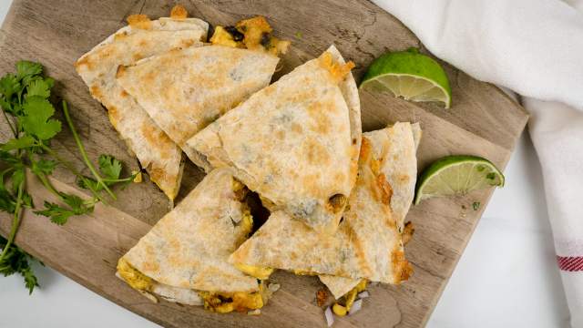 Breakfast quesadillas with eggs, corn, black beans, and cilantro on a cutting board.