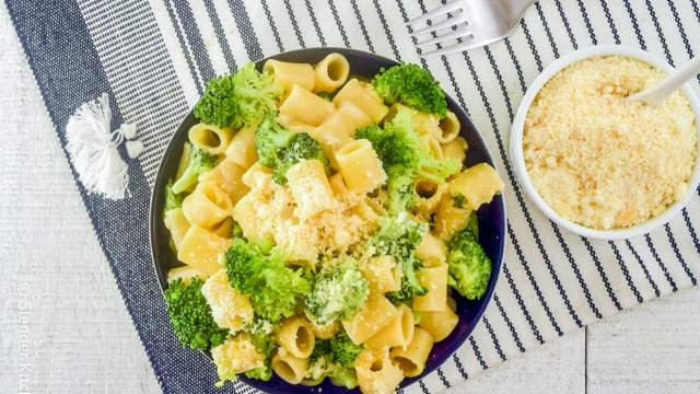 Broccoli pasta in a bowl with creamy parmesan sauce and Parmesan cheese on the side.