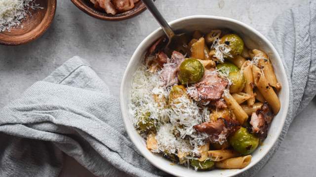 Brussels sprout pasta with bacon and Parmesan cheese in a bowl with a spoon.