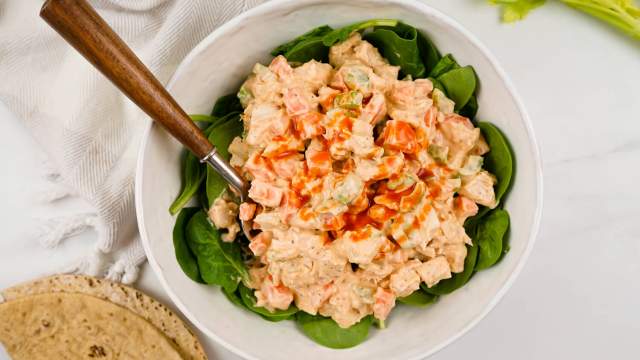 Buffalo chicken salad with fresh spinach, a whole wheat wrap, and a spoon in a bowl.