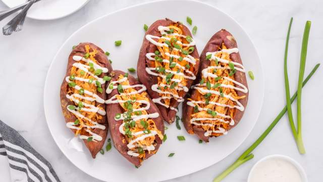 Buffalo chicken stuffed sweet potatoes on a plate with ranch dressing and green onions.