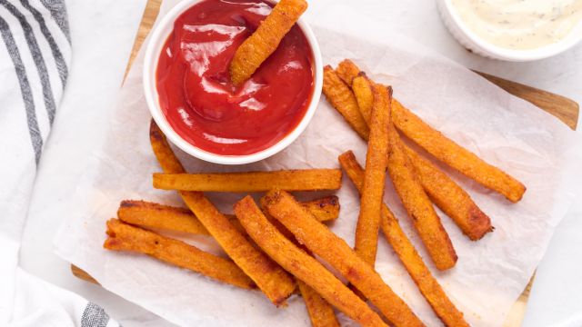 Butternut squash fries baked until crispy and served on parchment paper with ketchup and herb sauce.