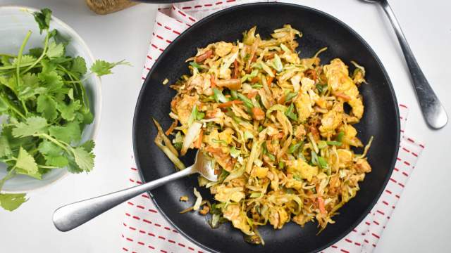 Cabbage fried rice with shredded cabbage, carrots, green onions, eggs, and soy sauce on a black plate.