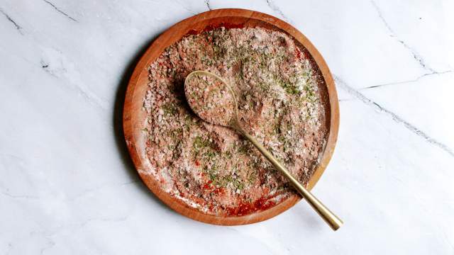 Cajun seasoning blend with smoked paprika, garlic powder, onion powder, oregano, and thyme on a wooden plate with a gold spoon.