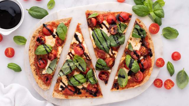 Caprese flatbead with cherry tomatoes, fresh mozzarella, basil leaves, and balsamic vinegar cut into four slices.