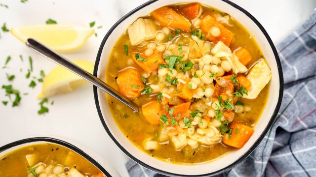 Chicken sweet potato soup with Israeli couscous in a bowl with lemon and parsley.