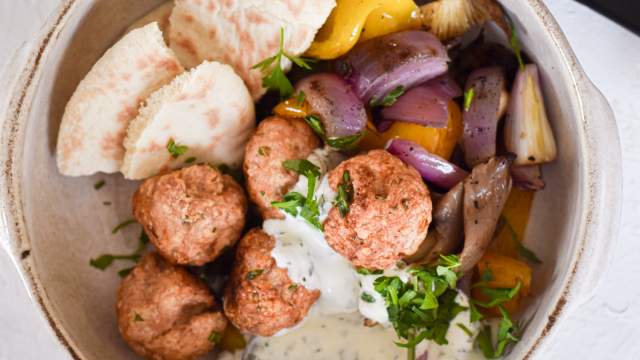 Chicken feta meatballs with fresh herbs in a bowl with tzatziki and grilled onions.