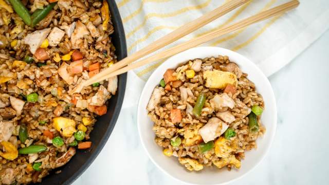 Chicken fried rice in a bowl with eggs, peas, carrots, chicken, and green beans with chopsticks.