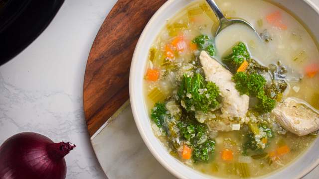 Slow cooker chicken quinoa soup with kale, carrots, celery, and onions in a bowl with a spoon.