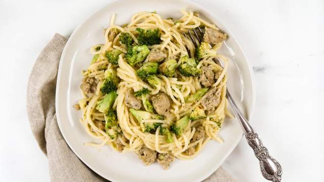 Chicken sausage pasta with broccoli on a plate with parmesan cheese and a fork.