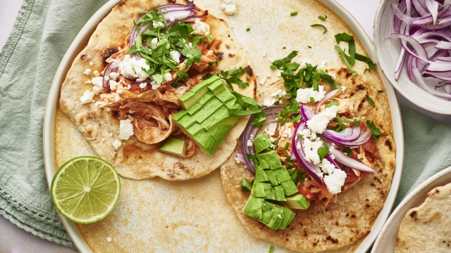 Chicken tinga tacos served on corn tortillas with queso fresco, cilantro, lime, and red onion.