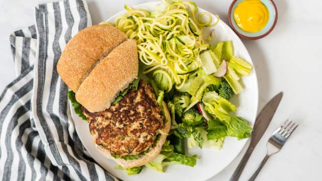 Chicken zucchini burgers on a plate with fresh herbs and ricotta cheese.