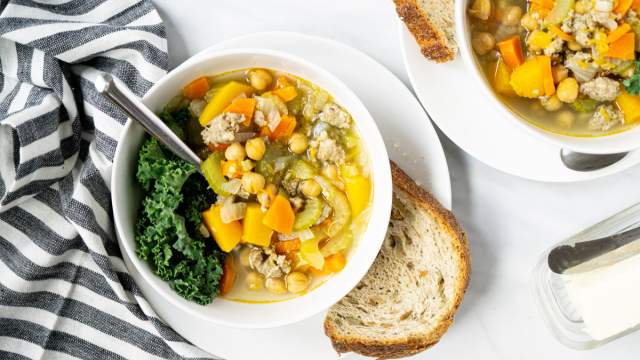 Chickpea stew with turkey sausage and butternut squash in a white bowl with bread on the side.