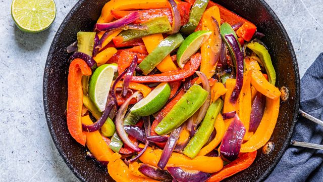 Chipotle fajita veggies with bell peppers and red onions in a skillet with lime wedges. 