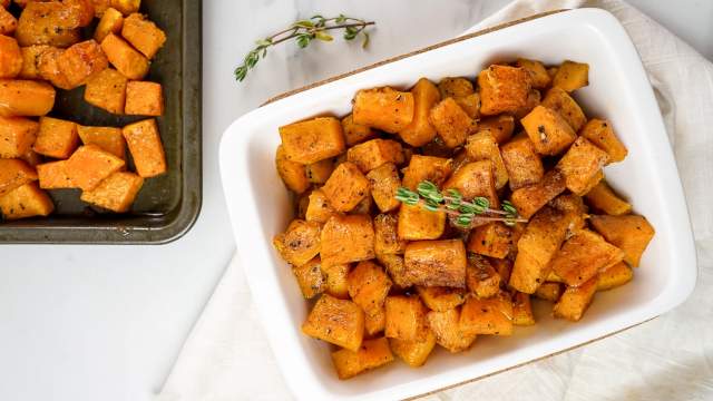 Cinnamon roasted butternut squash in a white dish with a baking sheet. 