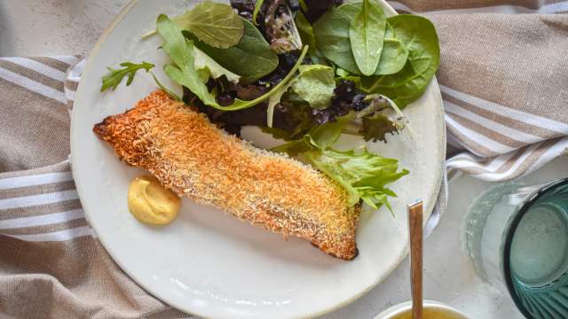 Coconut crusted salmon coated with crispy shredded coconut and spices on a plate with a mixed green salad.