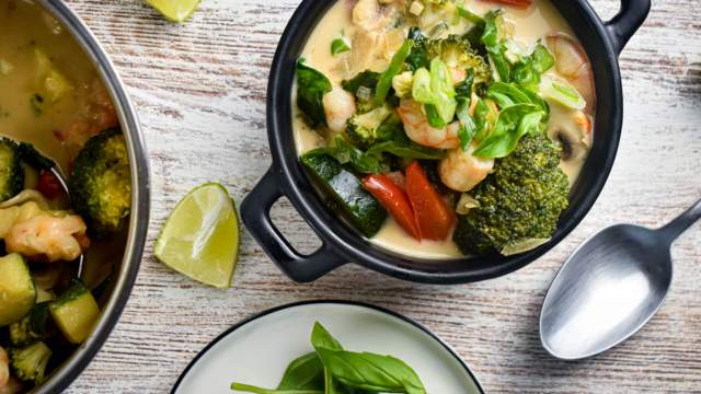 Coconut curry shrimp in a bowl with fresh vegetables, basil, green onions, and lime.