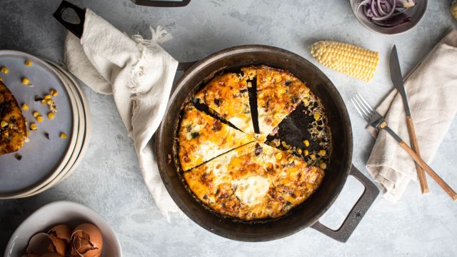 Corn and bacon frittata cooked with eggs, bacon, red onion, corn, and jalapeno in a skillet and sliced. 