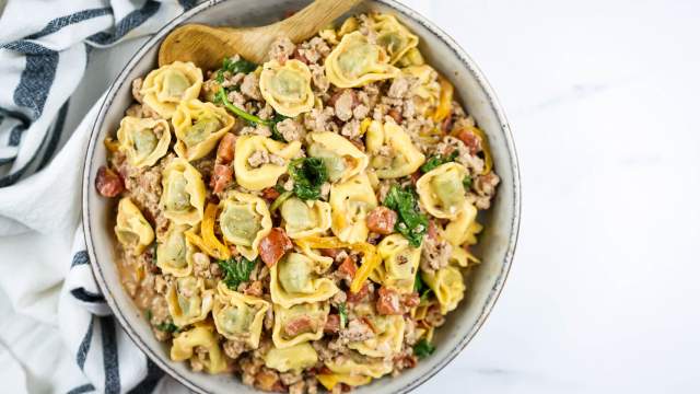 Creamy chicken tortellini in a creamy tomato sauce with fresh spinach in a bowl with a wooden spoon.