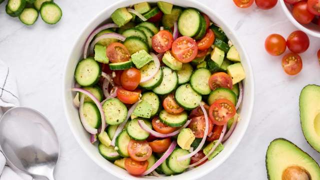 Cucumber salad with tomatoes, avocado, red onion, and vinaigrette in a large bowl.