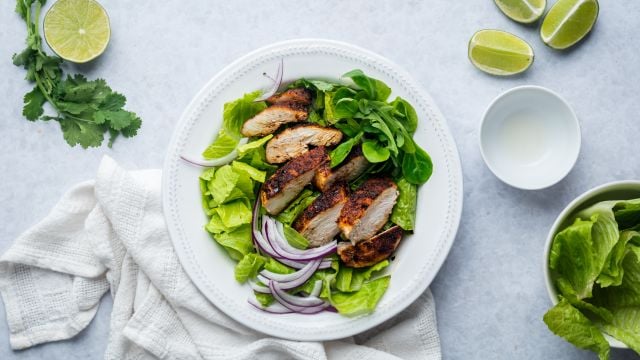 Cumin chicken breast with a homemade spice rub that's sliced and served with lime and salad greens.