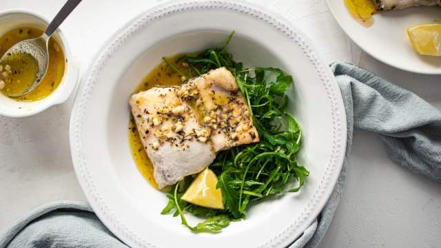 Easy baked cod with a lemon, garlic, and butter sauce on a white plate with mixed greens.