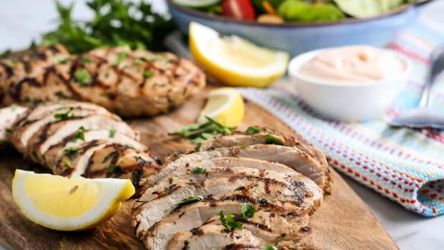 Grilled chicken breasts on a wooden cutting board with salad on the side.