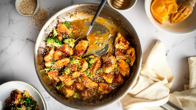 Easy orange chicken with broccoli served in a skillet with sticky sauce and sesame seeds.