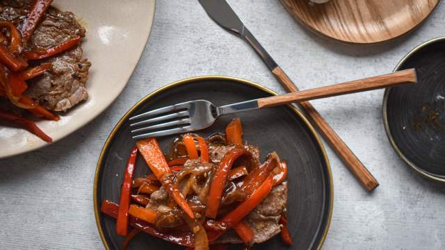 Pepper steak with thinly sliced sirloin steak, bell peppers, onions, and a peppery stir fry sauce on a plate with rice. 