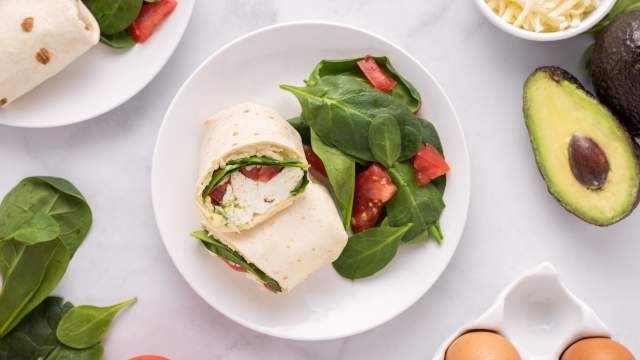 Egg white breakfast sandwich with cooked egg whites, avocado, tomatoes, spinach, and mozzarella wrapped in a tortilla.