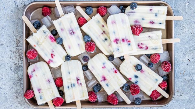 Fruit and yogurt popsicles with blueberries and raspberries on a tray with ice.