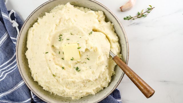 Cauliflower mashed potatoes with roasted garlic and butter in a ceramic bowl with a wooden spoon.