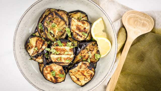 Grilled eggpplant with garlic, lemon, and parsley on a ceramic plate.