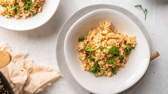 Garlic parmesan cauliflower rice with fresh parsley in a bowl with a wooden fork. 