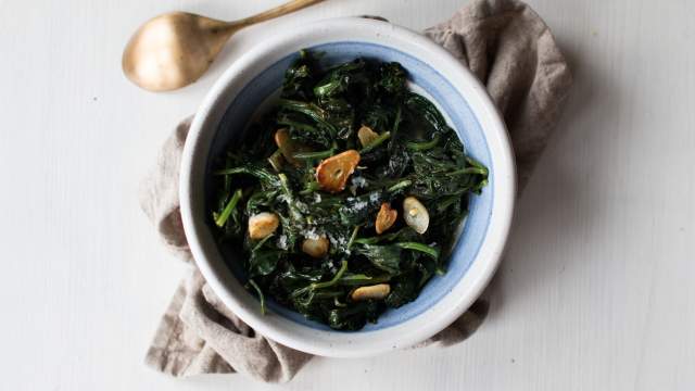 Garlic sautéed spinach with crispy garlic, black pepper, lemon, and sea salt on a white plate. 