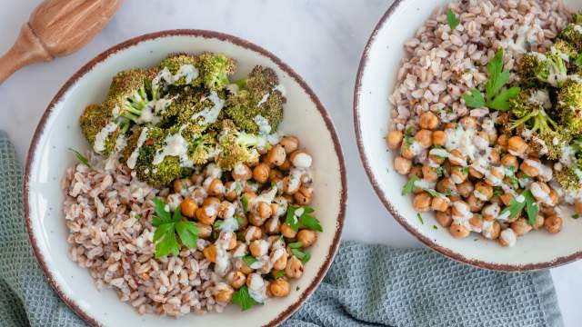 Garlic tahini broccoli bowls with cooked farro, roasted broccoli, roasted chickpeas, and tahini sauce in two bowls.