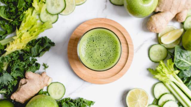 Green juice made with cucumbers, celery, kale, spinach, green apples, ginger, and lime juice in a glass.