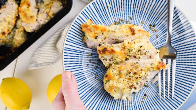 Baked Greek Yogurt Parmesan Chicken with herbs, lemon juice, Parmesan cheese, and garlic on a blue plate.