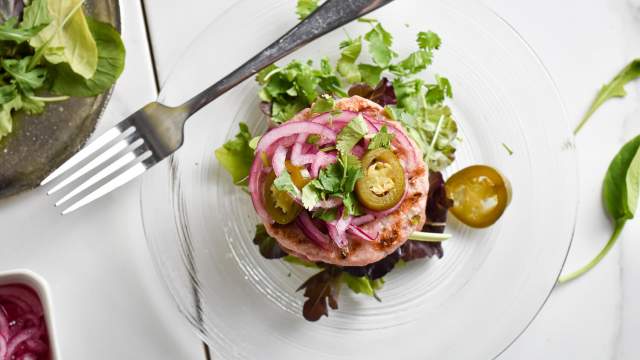 Green chile turkey burger with pickled red onions and greens on a plate with pickled jalapenos.