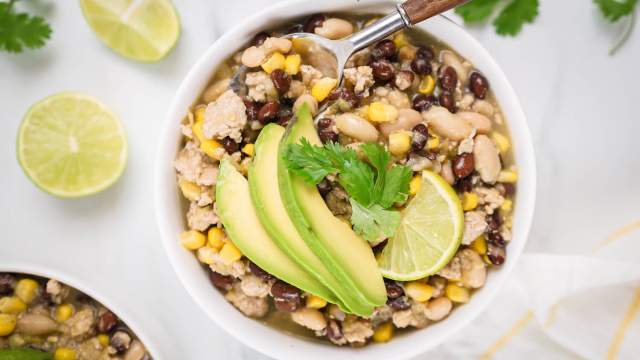 Green turkey chili with ground turkey, black beans, white beans, corn, and sliced avocado in a bowl.