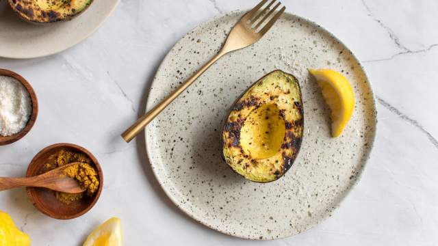 Grilled avocados on a plate with olive oil, lemon, salt, and pepper.