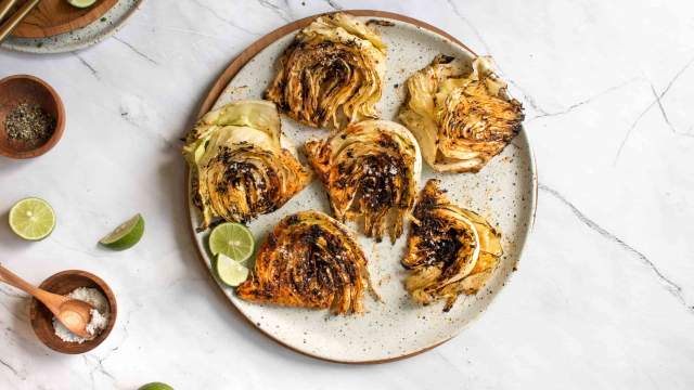 Grilled cabbage slices on a plate with grill marks with limes, salt, and grill seasoning. 