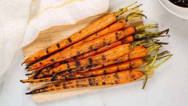 Grilled carrots with charred grill marks on a cutting board with sauce on the side.