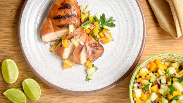 Grilled chicken with peach and cucumber salsa sliced on a plate.