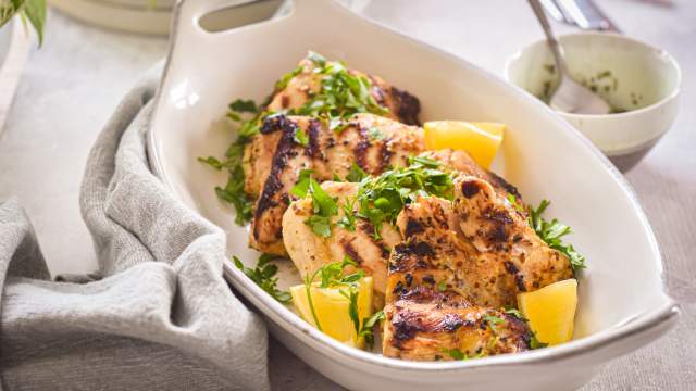 Grilled lemon dijon chicken thighs with fresh lemon and parsley in a white dish with a linen napkin.