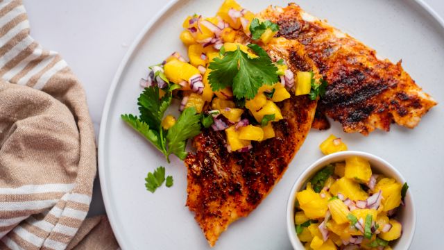 Grilled mahi mahi with paprika spice rub and pineapple salsa served on a white plate.