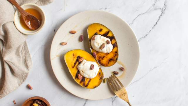 Grilled mango sliced in half on a plate with a dollop of yogurt, honey, and pistachios.