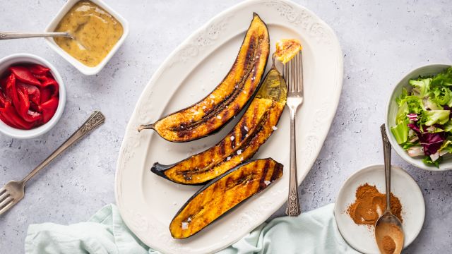 Grilled plantains with dark brown grill marks on a plate with cinnamon on the side.