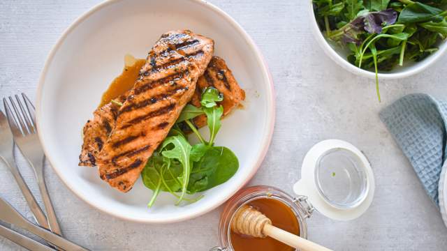 Grilled honey and lime salmon on a plate with sauce and a salad on the side.