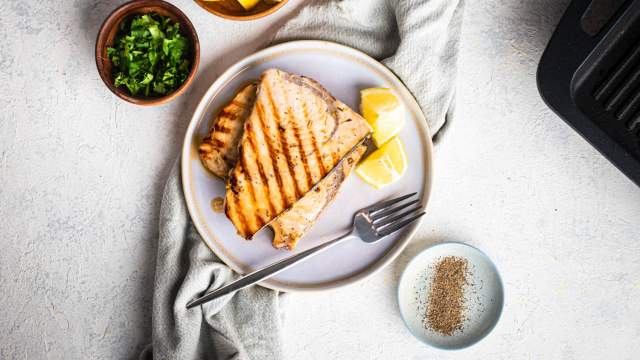 Grilled swordfish with garlic, lemon, and herbs on a plate with fresh parsley.